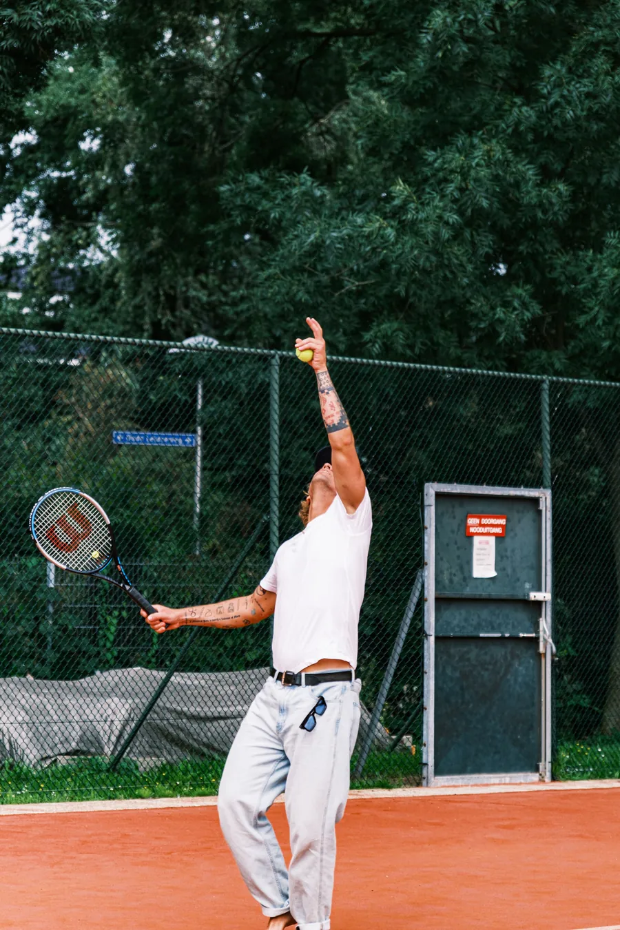 Club player tossing the ball to serve with a Wilson racket on clay